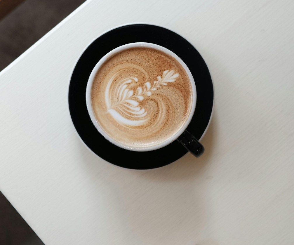 Hot latte with steamed milk and leaf-shaped latte art in a black cup
